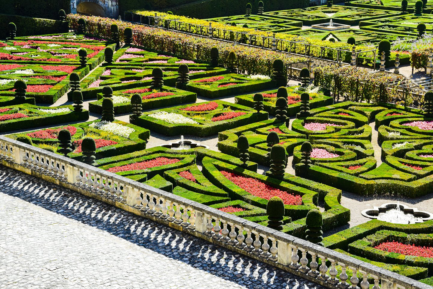 Jardín formal con setos geométricos y parterres de flores coloridas.