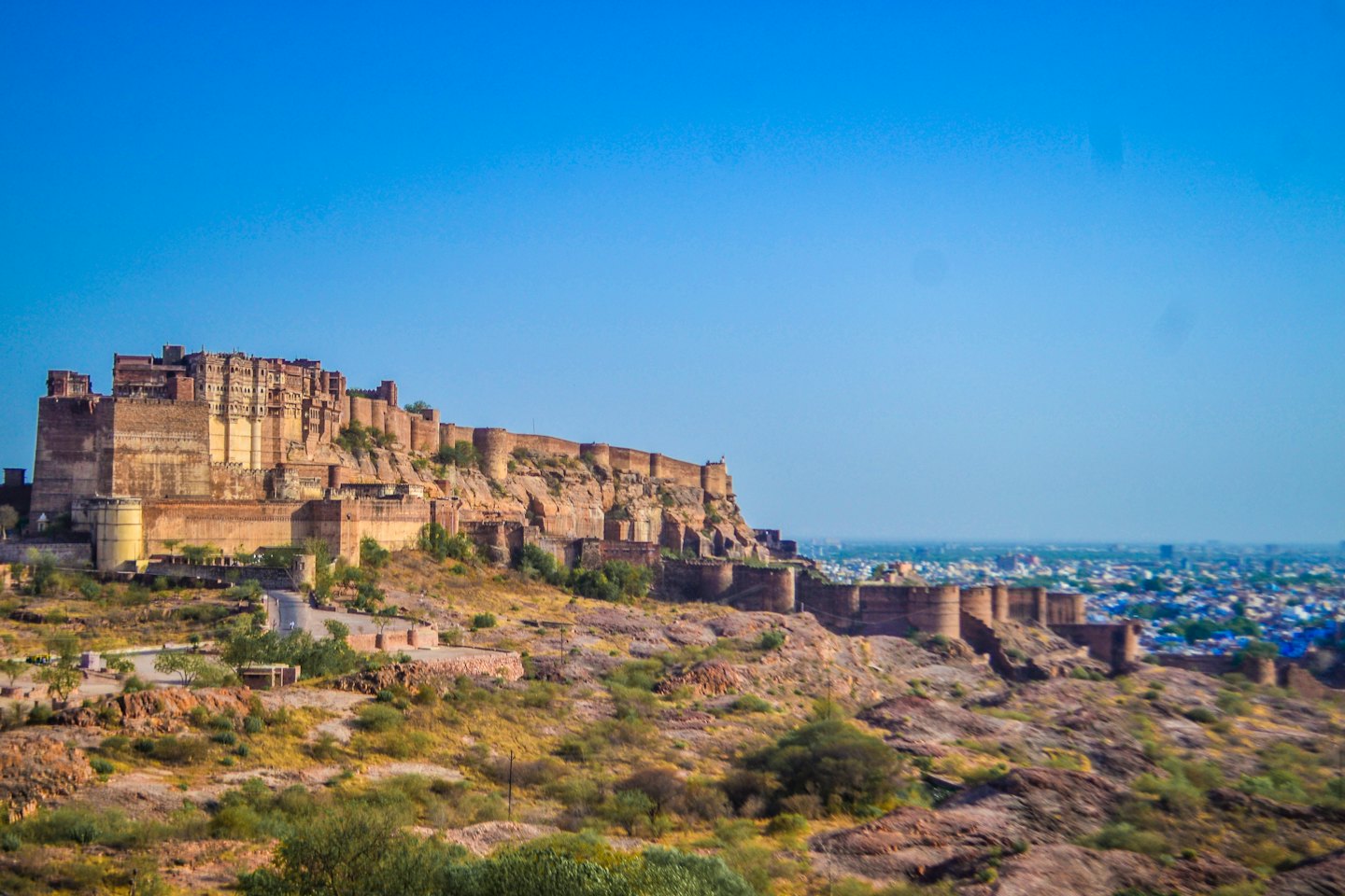 Antigua fortaleza en colina árida con vistas a ciudad de tejados azules.