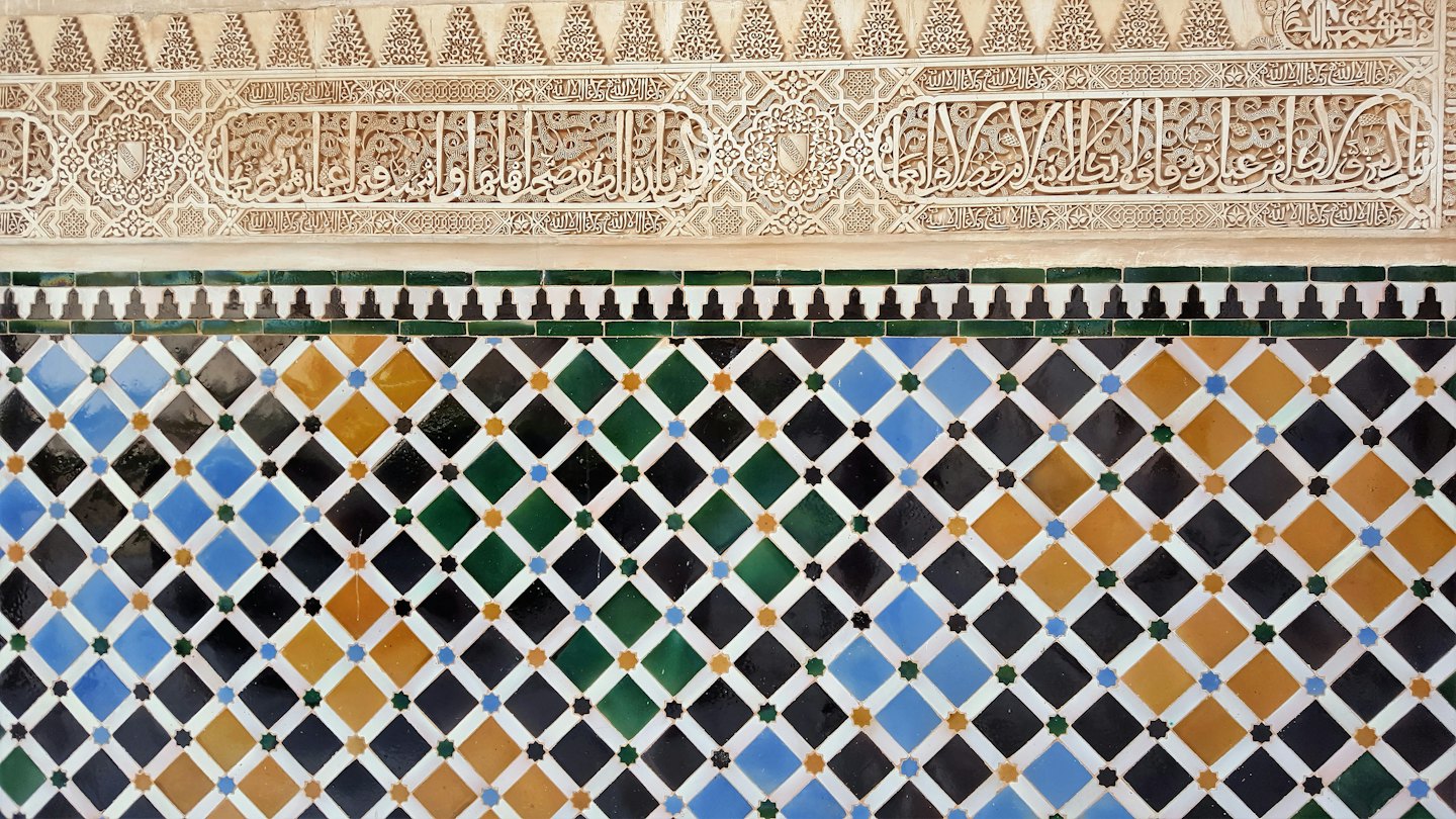 Detallados relieves de yeso de estilo morisco sobre coloridos patrones de azulejos geométricos.